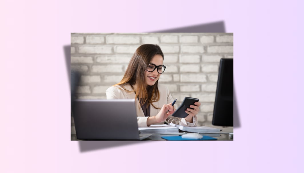 A woman doing some calculations with a calculator in her hand, and a laptop on the table.